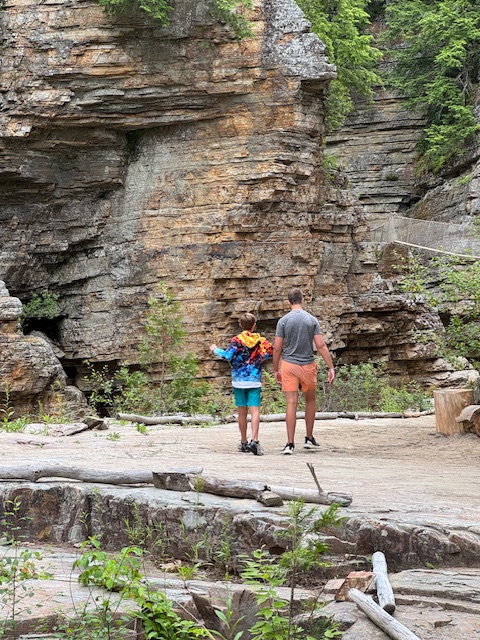 Two boys, one younger, one older are walking away from the camera through a canyon.